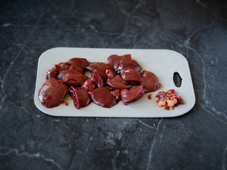 Процесс очистки и нарезки куриной печени на белой доске